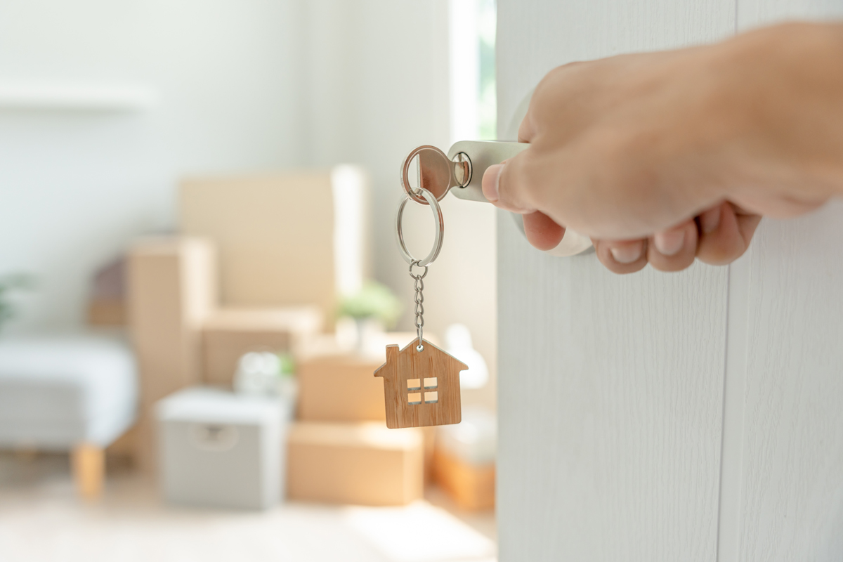 Umzug. Der Schlüssel steckt in der Tür eines Hauses oder einer Wohnung. Im Zimmer sind Kartons und Möbeln.