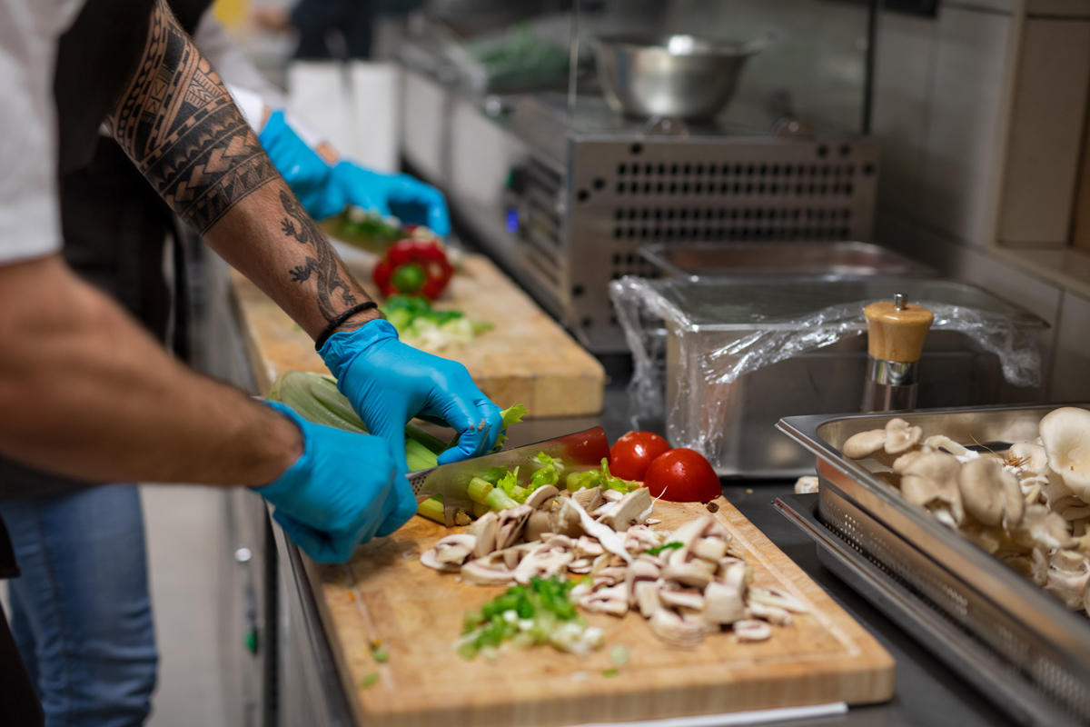 Koch mit Handschuhen, der drinnen in der Restaurantküche Gemüse schneidet.