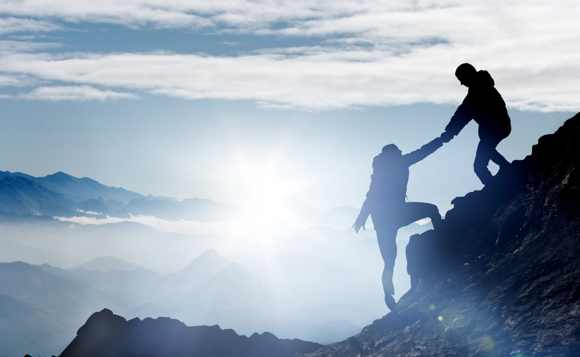 Zwei Menschen beim Bergsteigen und einer davon reicht dem Anderen die Hand und zieht ihn hoch