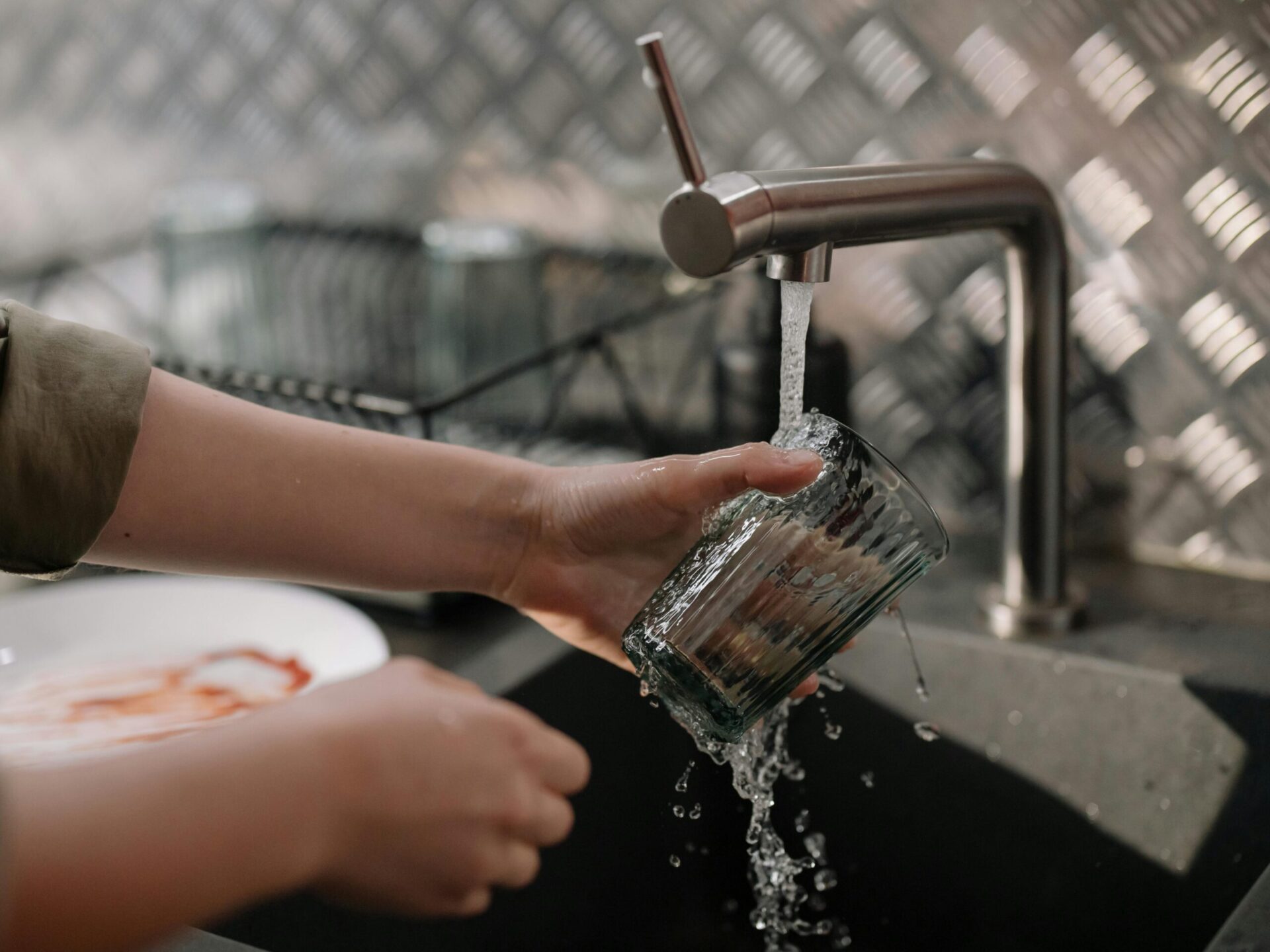 Ein Glas wird unter das fließende Wasser eines Wasserhahns gehalten