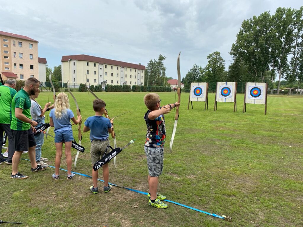 Kinder und Männer schießen mit einem Bogen auf Zielscheiben