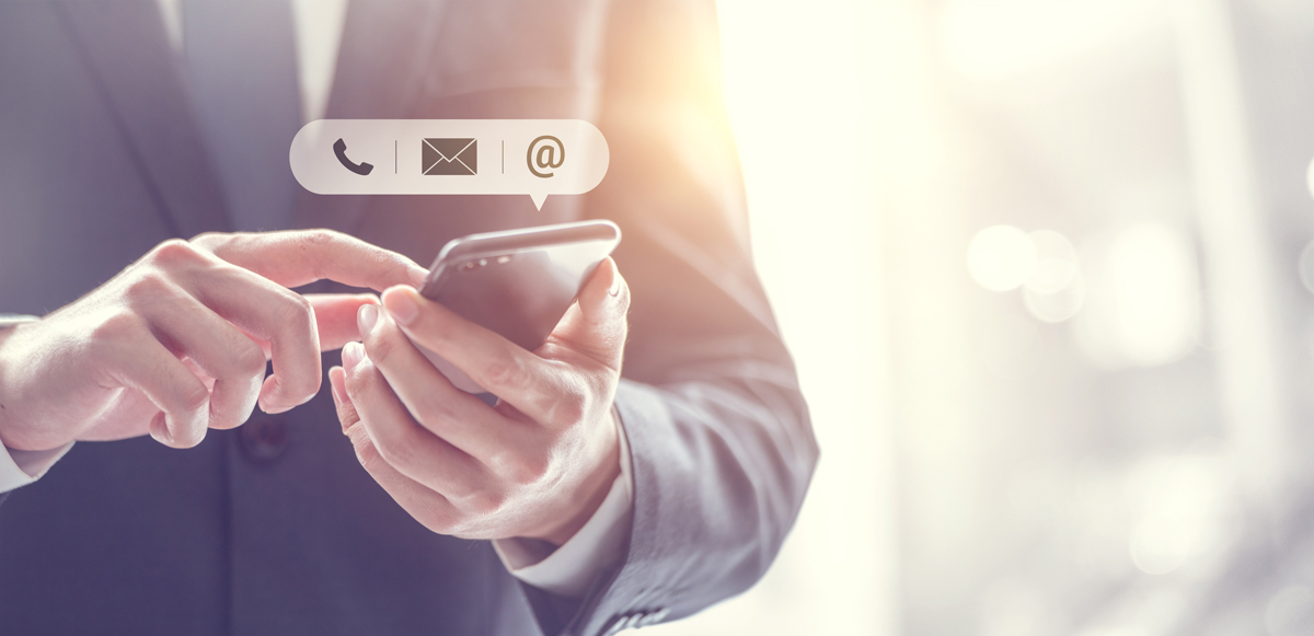 Person im Anzug tippt auf seinen Smartphone - über sein Smartphone erscheinen Icons von einem Telefon, Brief und dem At-Zeichen