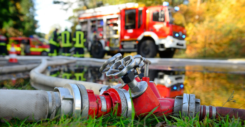 Feuerwehreinsatz im Wald - Feuerwehrauto im Hintergrund davor Wasserschläuche