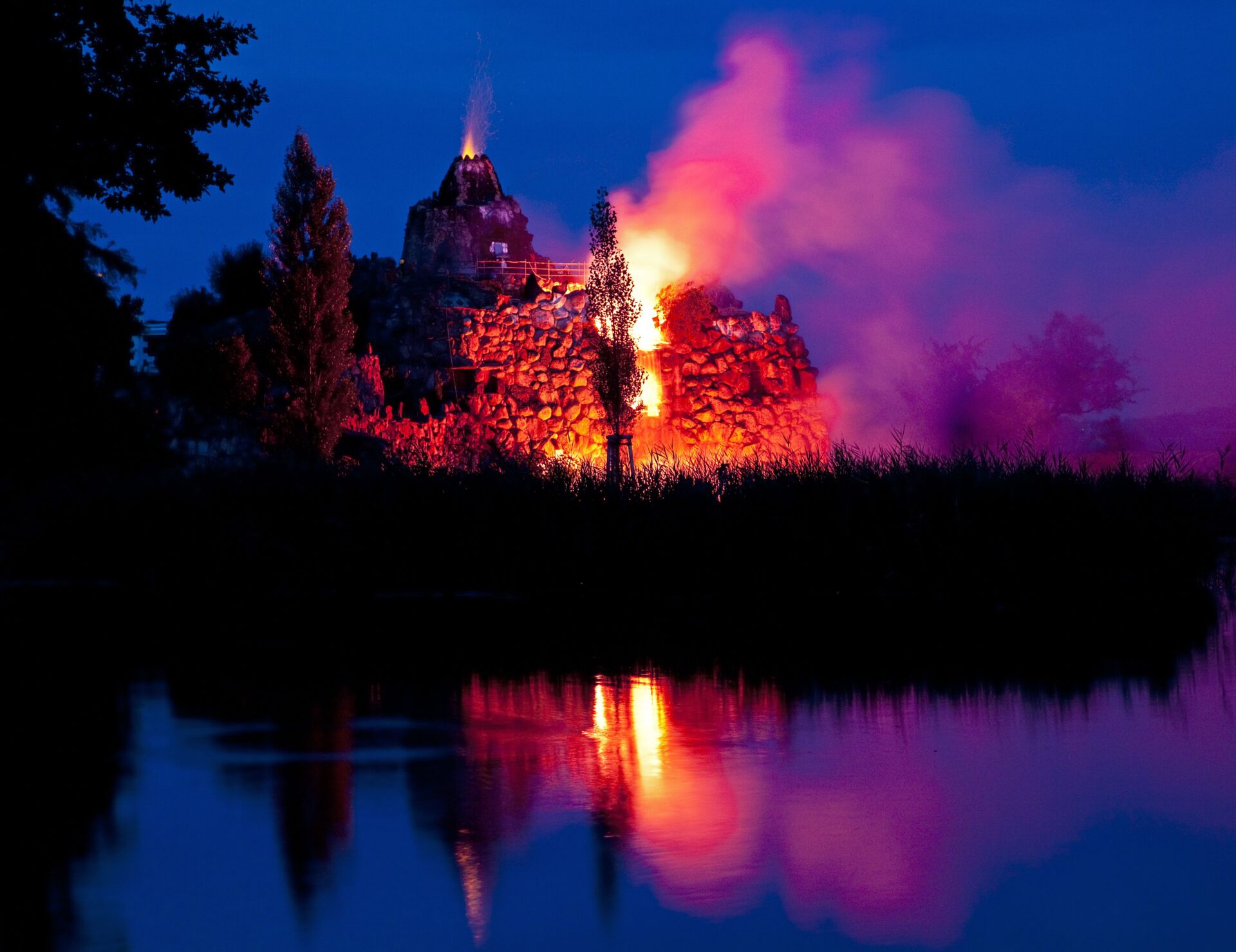 Inszenierter Vulkanausbruch auf der Insel Stein im Wörlitzer Park bei Nacht – Feuer, Rauch und Funken spiegeln sich im Wasser