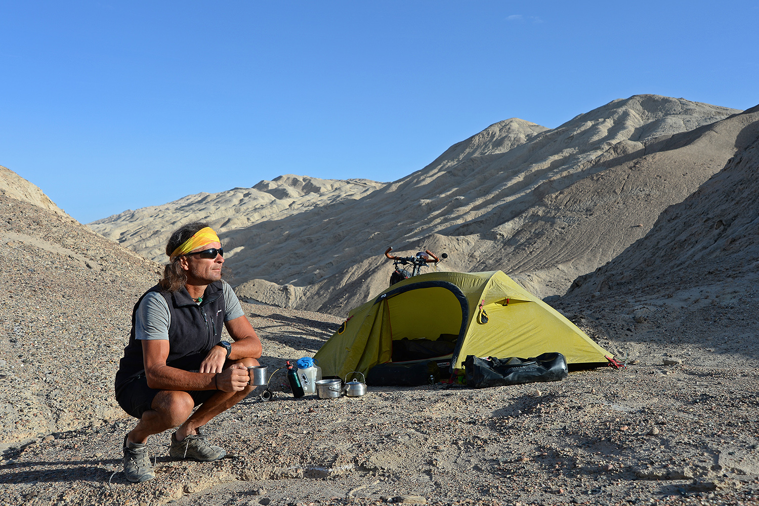 Thomas Meixner sitzt in einer bergigen Landschaft in Westchina neben einem gelben Campingzelt.