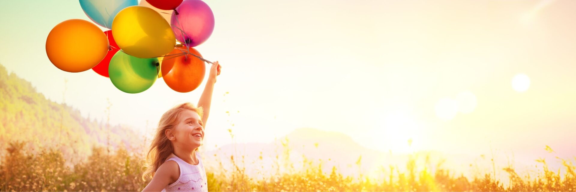 Kind läuft mit Luftballons über die Wiese bei Sonnenschein