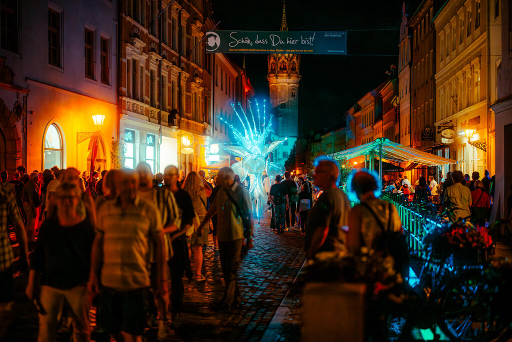 Nachtszene, Menschen, die das Stadtfest Wittenberg besuchen, Banner auf dem steht "schön, dass du da bist"