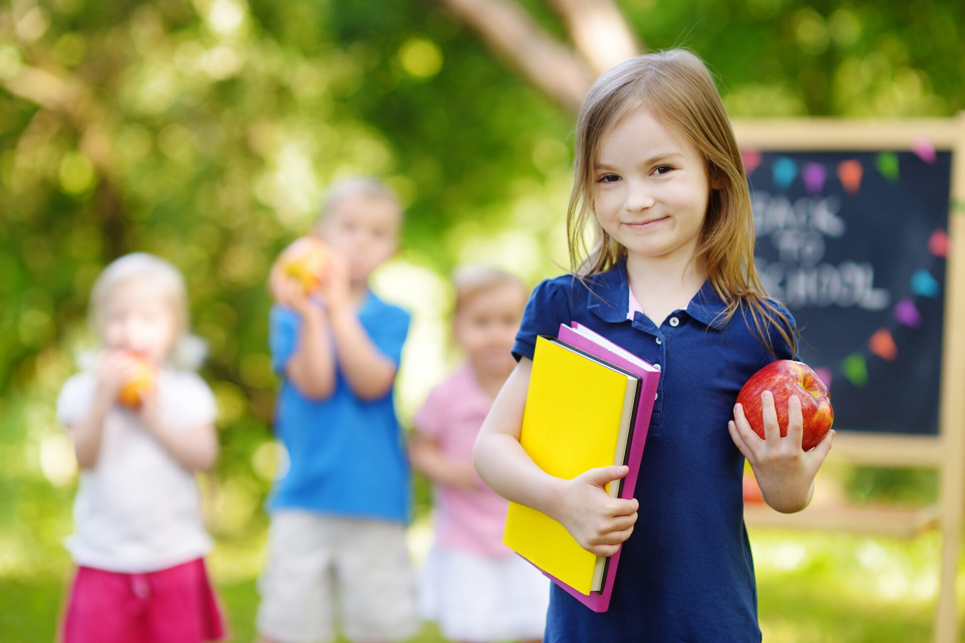 Ein Mädchen hält Schulbücher und einen Apfel in der Hand