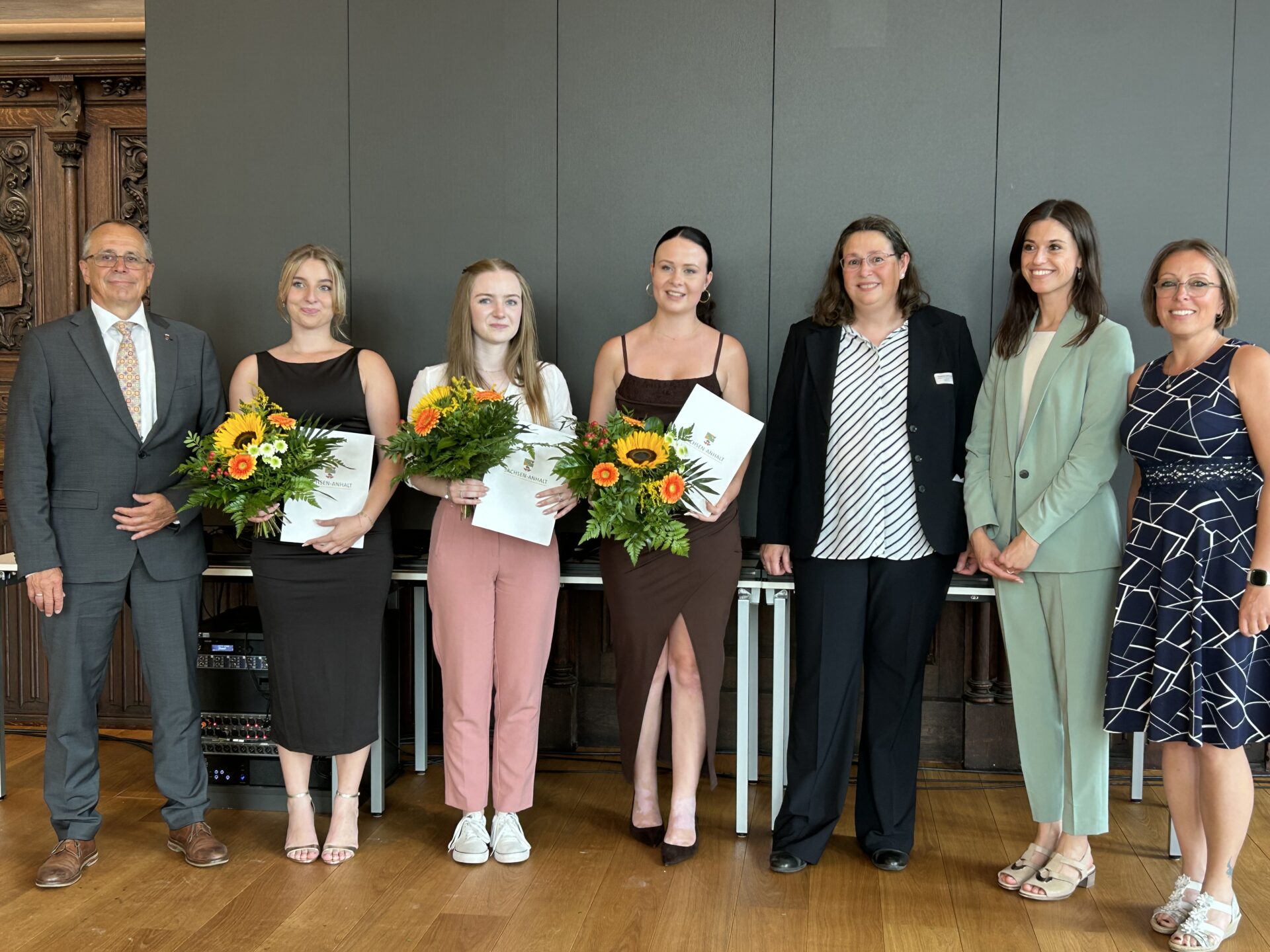 Sieben Personen, zum Teil mit Zeugnissen und Blumen in der Hand, lassen sich fotografieren.