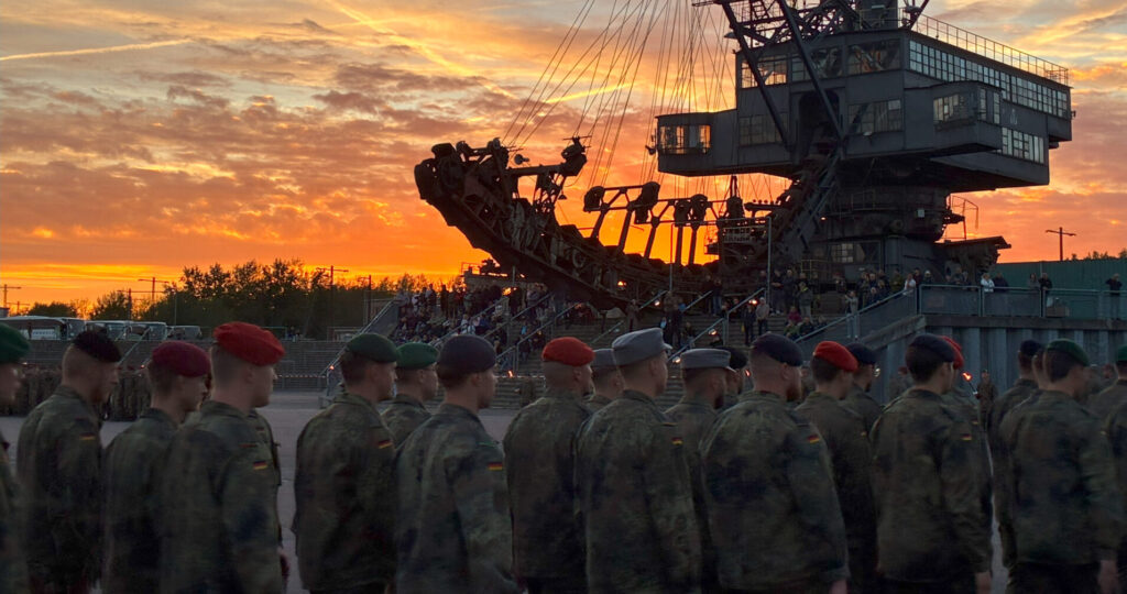 Eine Gruppe von unteroffizieren läuft ein. Im Hintergrund ist ein großer Bagger zusehen. Es ist Abendstimmung.