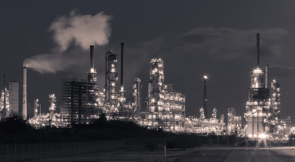 Beleuchtete Industrieanlage mit mehreren hohen Schornsteinen und rauchendem Schornstein in der Nacht - Landkreisversammlung