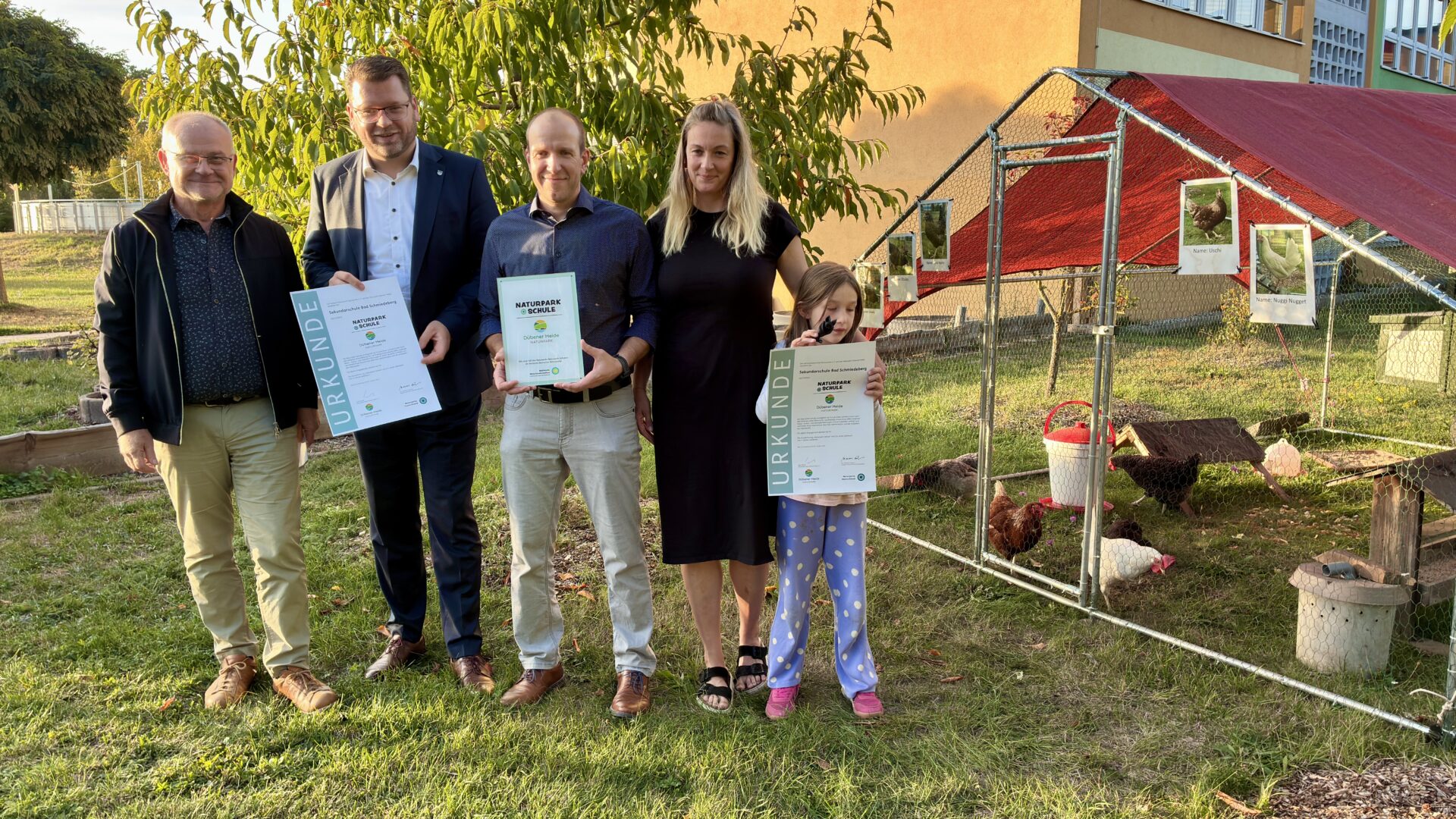 Vier Erwachsene und ein Kind halten Urkunden bzw. eine Auszeichnung in den Händen und lächeln in die Kamera bei der Zertifizierung zur Naturparkschule