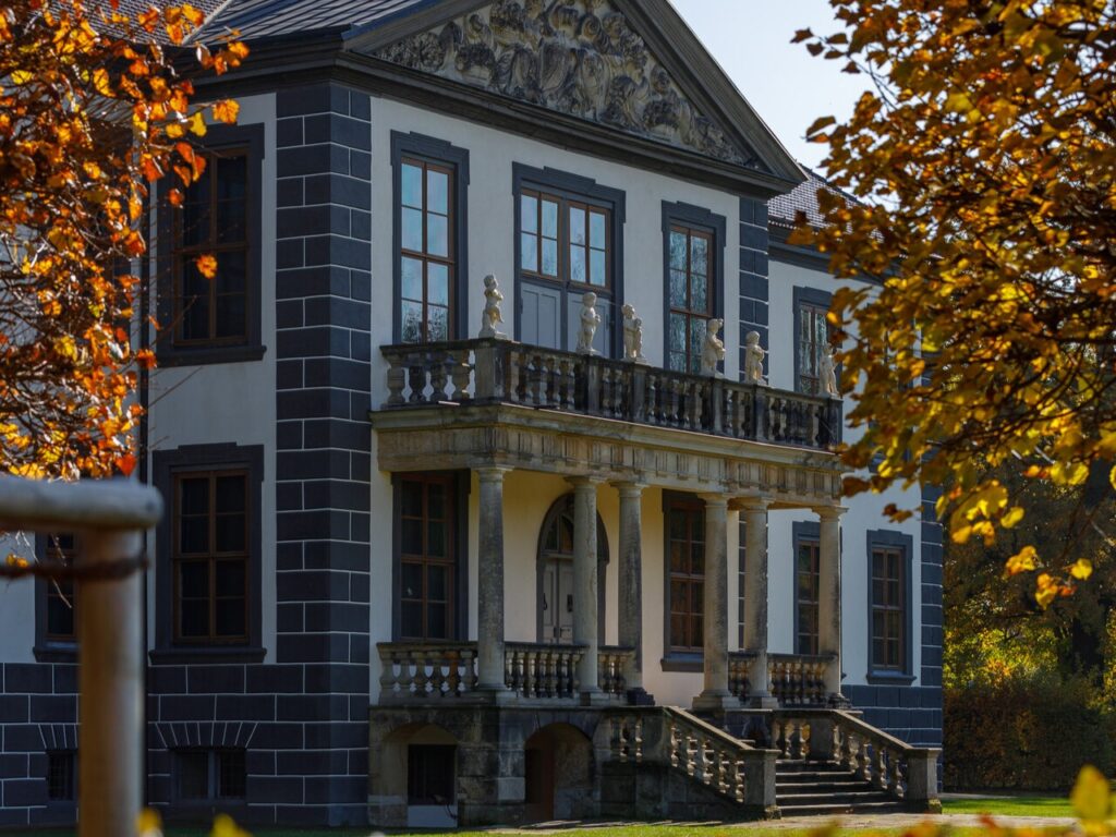 Barockes Schloss mit Säulenbalkon und Balustrade umgeben von herbstlich gefärbtem Laub