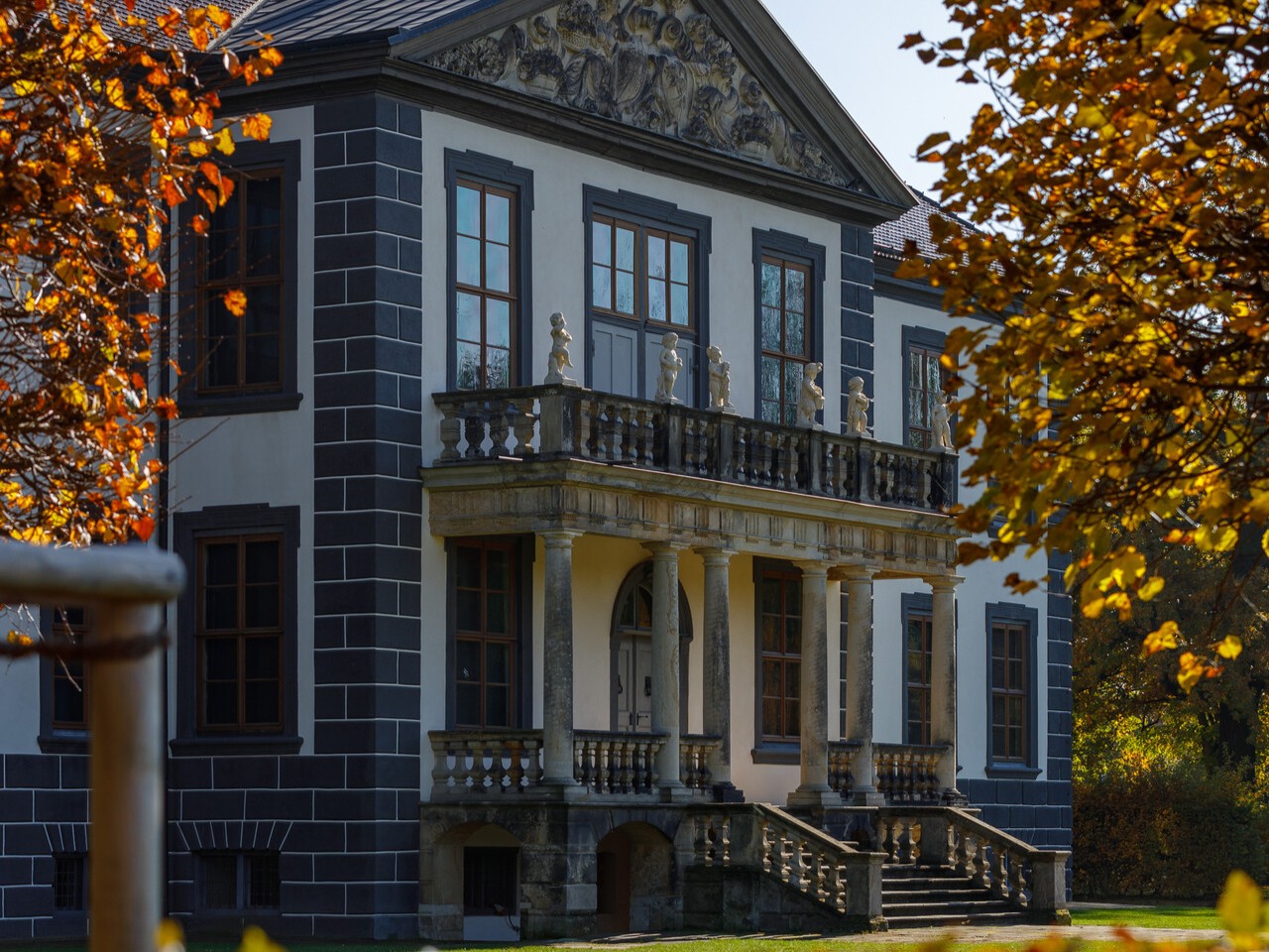 Barockes Schloss mit Säulenbalkon und Balustrade umgeben von herbstlich gefärbtem Laub