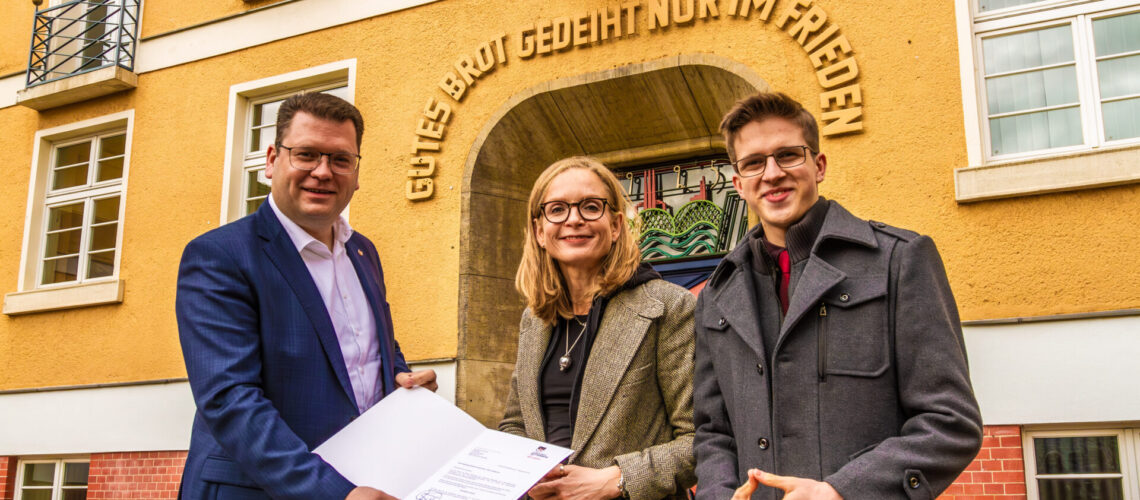 Landrat Christian Tylsch (links) übergibt Schulleiterin Anja Aichinger (Mitte) das offizielle Schreiben zur Umbenennung des Gymnasiums. Rechts im Bild: Schülersprecher Meldrick Stern.