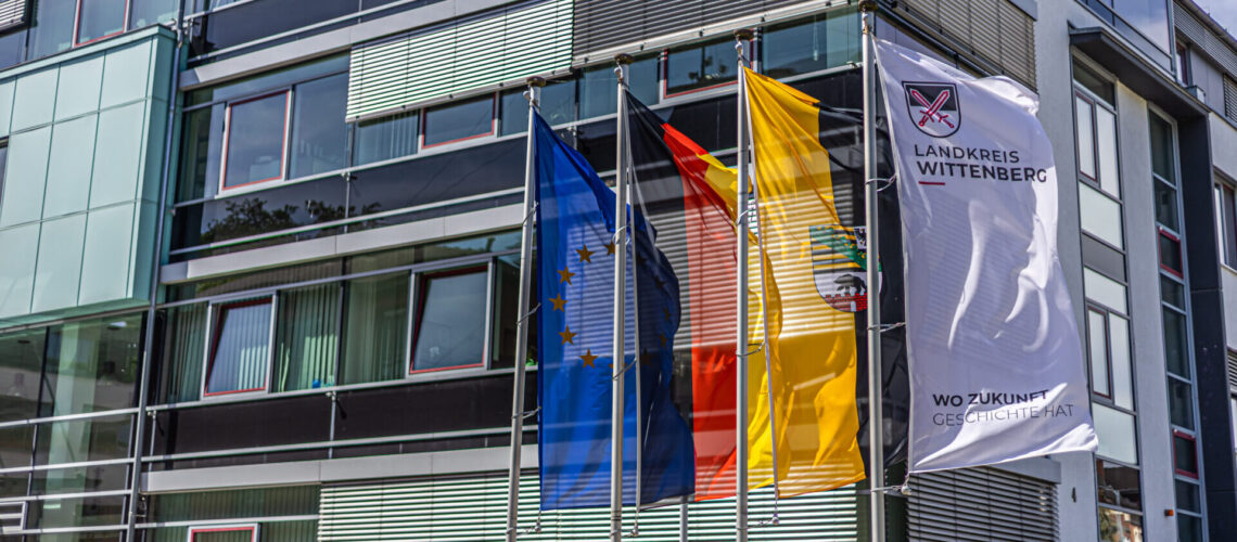 An der Kreisverwaltung hängen die (v.l.n.r.) die Europaflagge, die Bundesflagge, die Flagge des Landes Sachsen-Anhalt und die Fahne mit dem Logo und Claim der Kreisverwaltung Wittenberg.