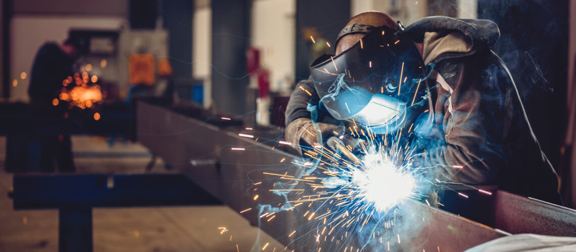 Schweißer arbeitet in der Halle an einem großem Metallstück.