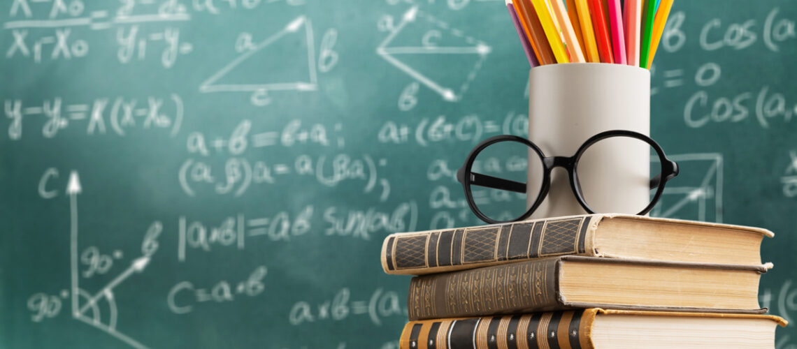 Schultafel mit Formeln davor stehen Bücher und Stifte