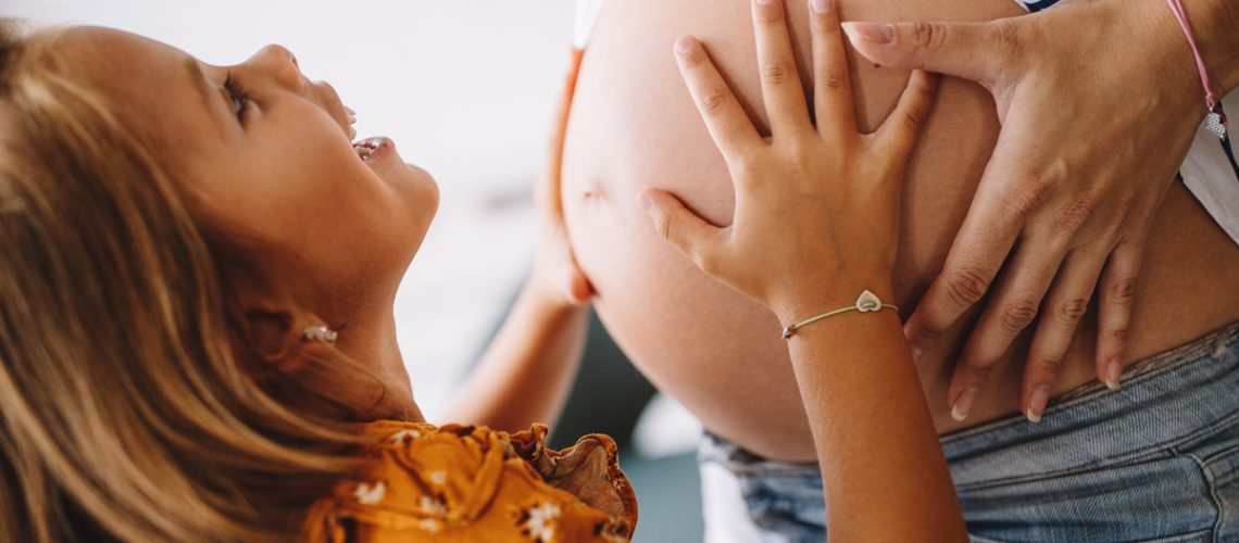 Schwangere Frau mit Tochter, die ihre Hände auf den Babybauch legt