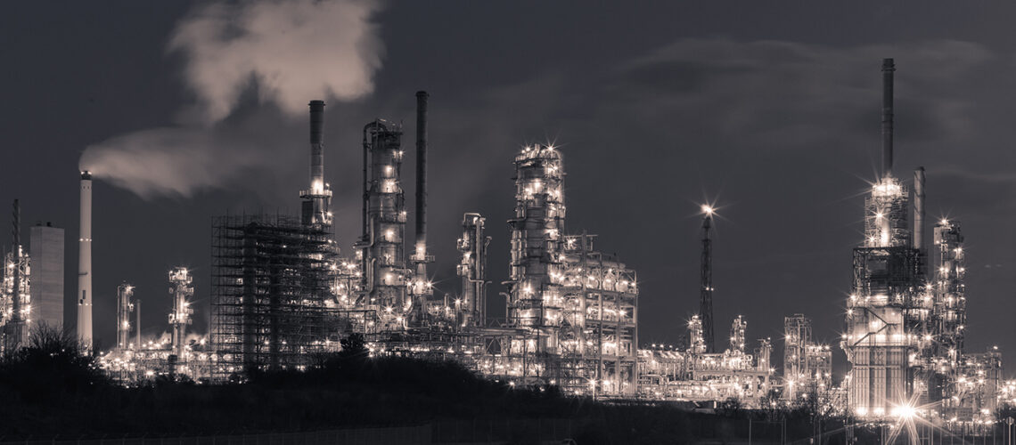 Beleuchtete Industrieanlage mit mehreren hohen Schornsteinen und rauchendem Schornstein in der Nacht - Landkreisversammlung