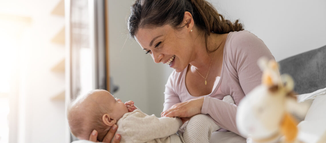 Mutter, die mit ihrem drei Monate alten Baby im Schlafzimmer spielt