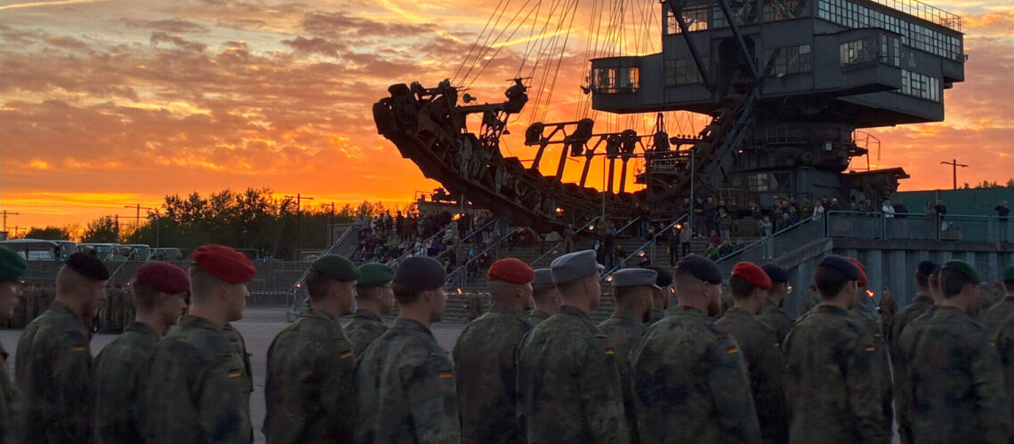 Eine Gruppe von unteroffizieren läuft ein. Im Hintergrund ist ein großer Bagger zusehen. Es ist Abendstimmung.