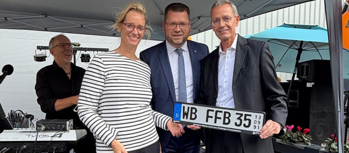 Drei Menschen halten ein Jubiläums-Nummernschild in den Händen.