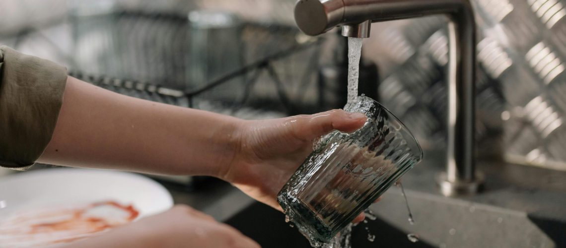 Ein Glas wird unter das fließende Wasser eines Wasserhahns gehalten