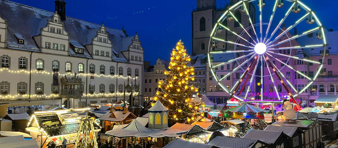 Wittenberger Weihnachtmarkt am späten Nachmittag - Man sieht das Riesenrad, den Weihnachtsbaum und die kleinen Hütten sowie das Rathaus und die Stadtkirche.