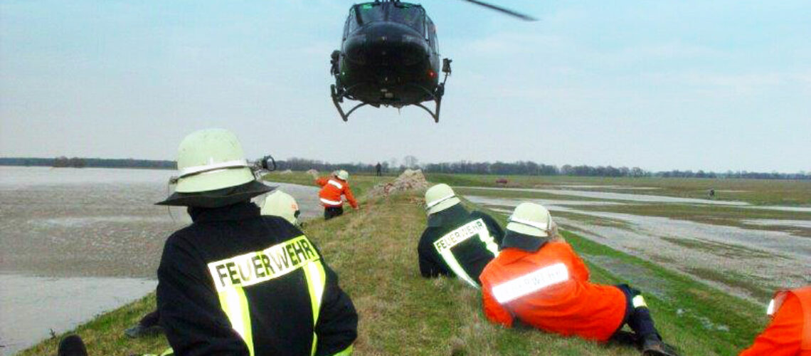 Hochwasser - Feuerwehrmänner sitzen auf dem Damm über ihnen fliegt ei